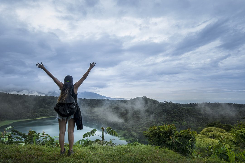 Kvinde står med løftede arme foran en kratersø i Costa Rica